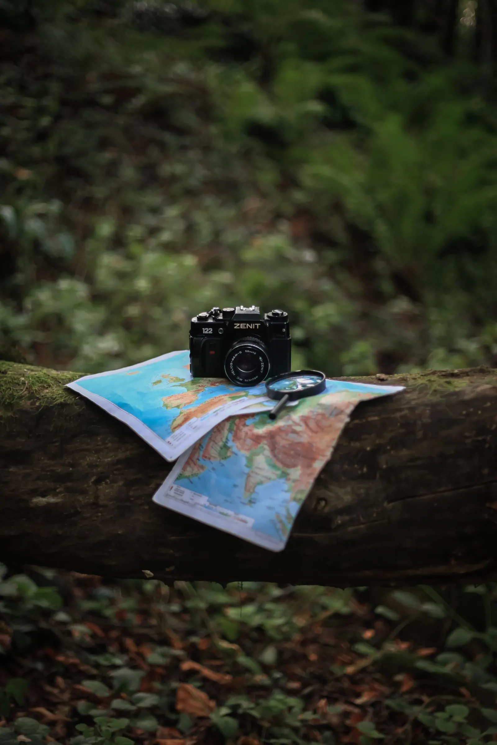Une carte, une loupe et un appareil photo posés en forêt
